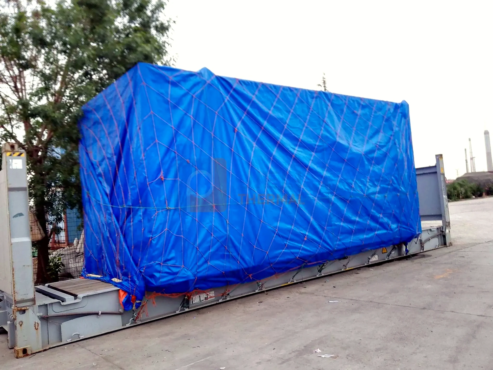Industrial boiler export delivery — tarped boiler package on a flat-rack container